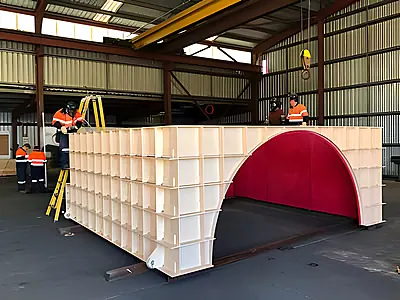 Workers assembling a large curved rock box chute transfer point structure at Rexline Engineering fabrication facility